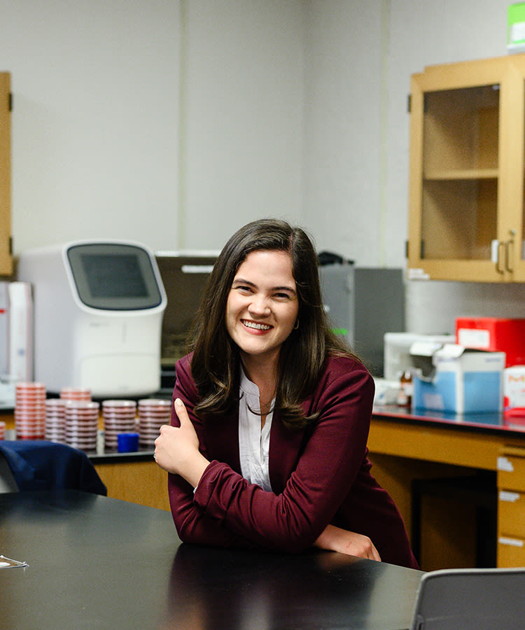 Sierra Rose wearing a suit jacket, leaning on a table and smiling in a CCU science lab