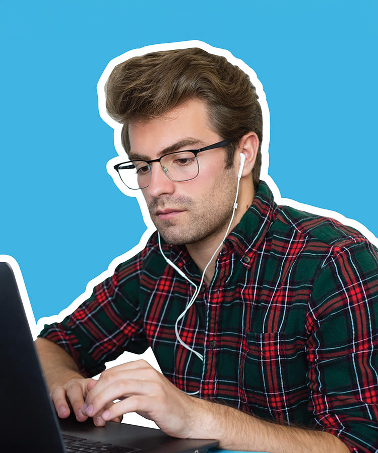 will witt sitting at a laptop with ear buds in and a bright blue background