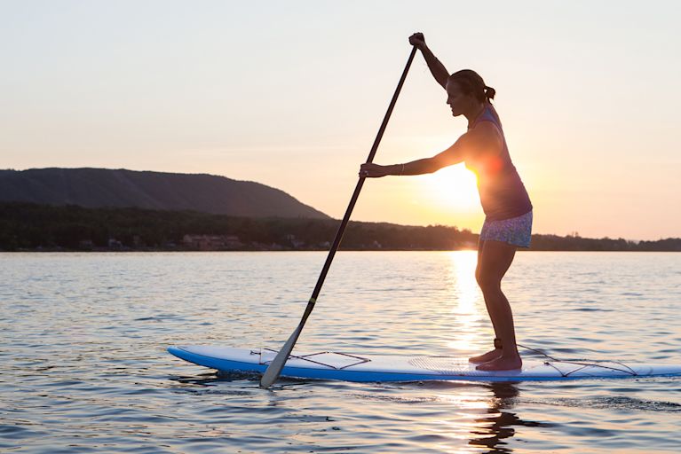 A woman is paddle boarding in the mountains to relieve stress.
