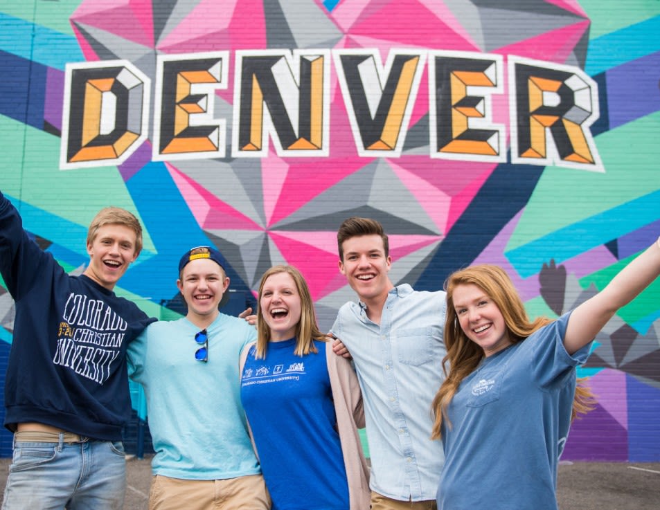 Students standing, arm in arm, in front of colorful mural in Denver, CO.