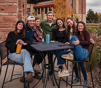 Several students sitting together around an outdoor table, with the CCU campus in the background.