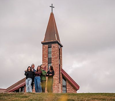 Young CCU students standing together on campus, with the chapel steeple visible in the background.