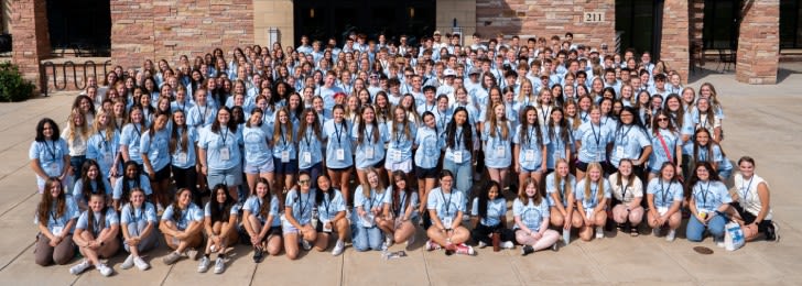 Large group of prospective students posing and smiling on CCU's campus in front of a brick building wearing matching shirts