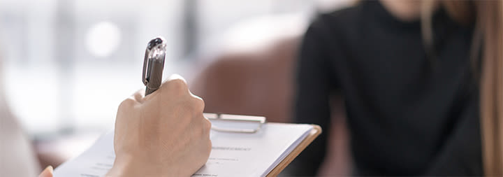 A hand holding a pen writes on a clipboard