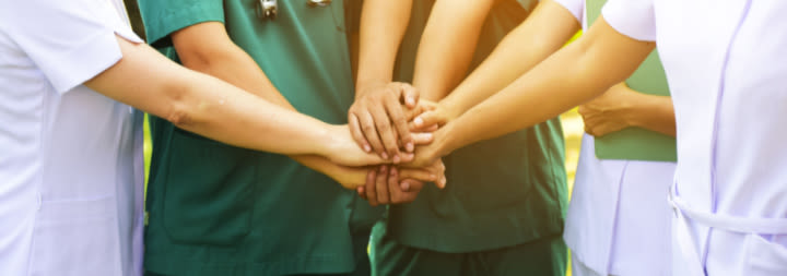 Nurses gathered together with their hands in the middle