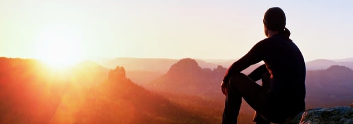 Male hiker looking out at mountain and sunrise.