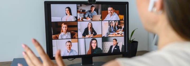 A woman sitting at a desk is on a large-group video call.