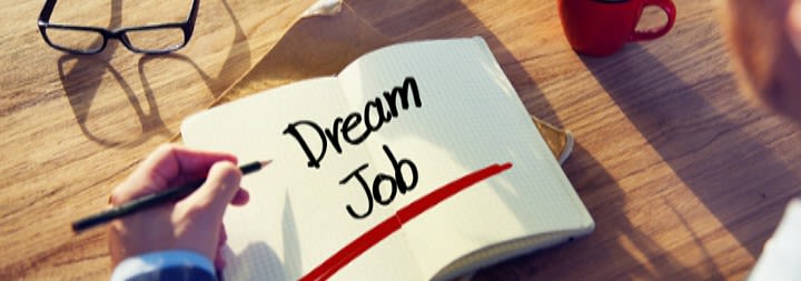 Book open on desk that says 'dream job' and man holding pen.