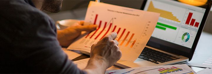 A man looks at a chart he holds in front of a laptop
