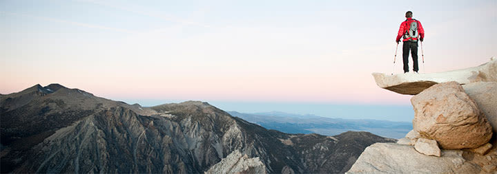 man climbing a mountain with walking sticks