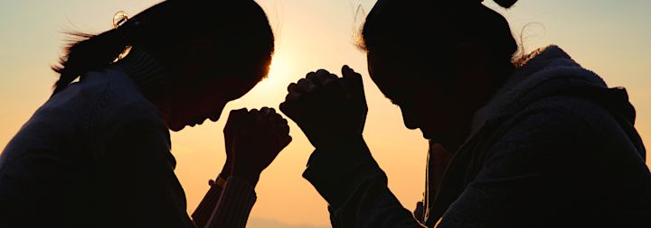 Two silhouettes pray together.