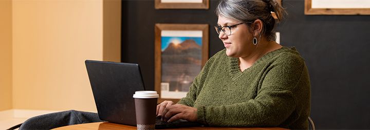 Woman working on laptop with a cup of coffee.
