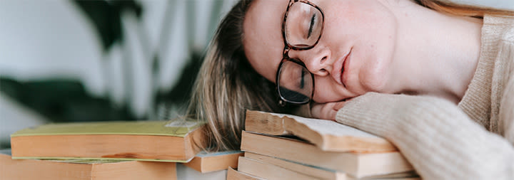 female student sleeping on a pile of books