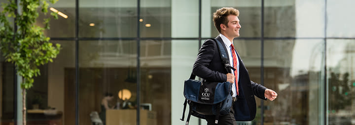 A business man with a laptop bag walks in a cityscape.