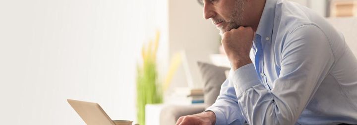 A professional businessman is sitting on a couch looking at a laptop.