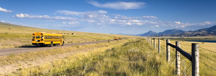 A school bus is driving through the country in a rural area.