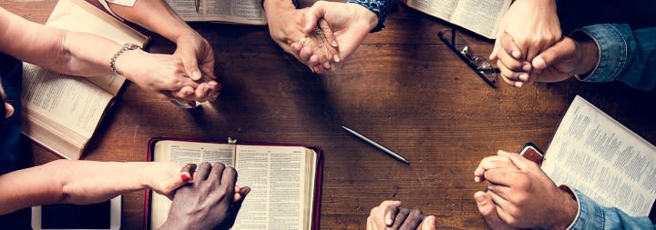 Adult students praying around a table.