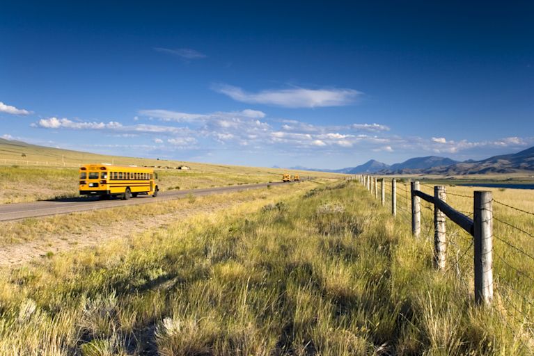 A school bus is driving through the country in a rural area.