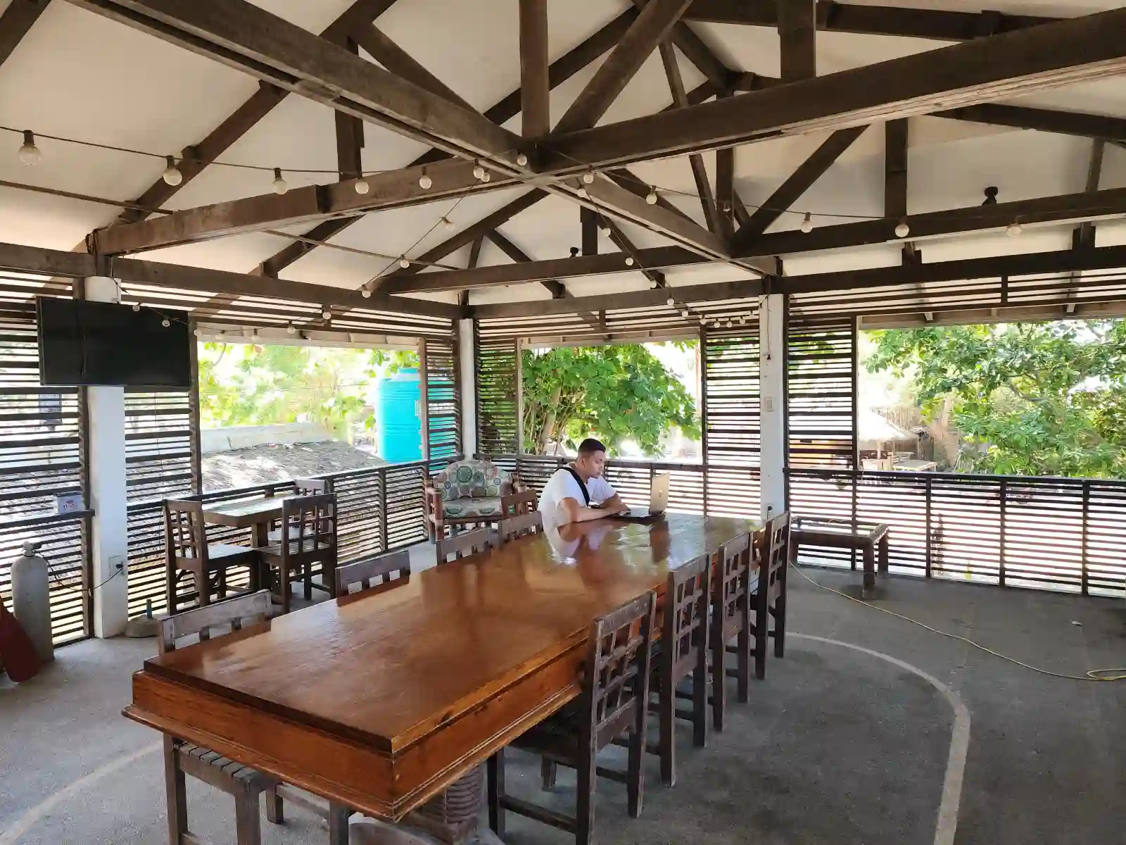 Person working on a laptop at a long wooden dining table on the open air second floor deck of Alfresco Beach Resort in Matabungkay Lian Batangas