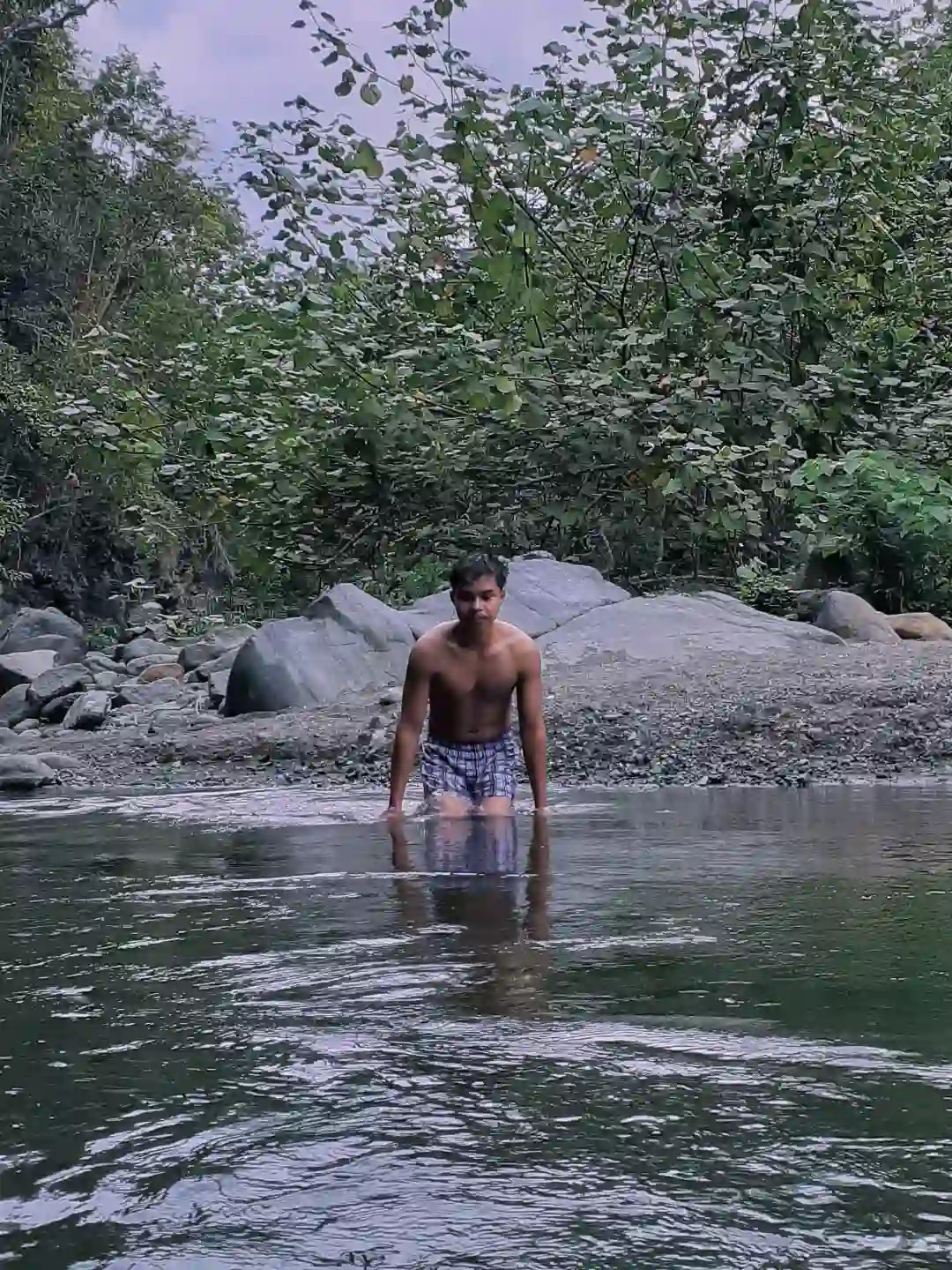 A young man wading knee deep in a clear rocky river with large boulders and green trees on the bank in Barangay Maputi San Isidro Davao Oriental