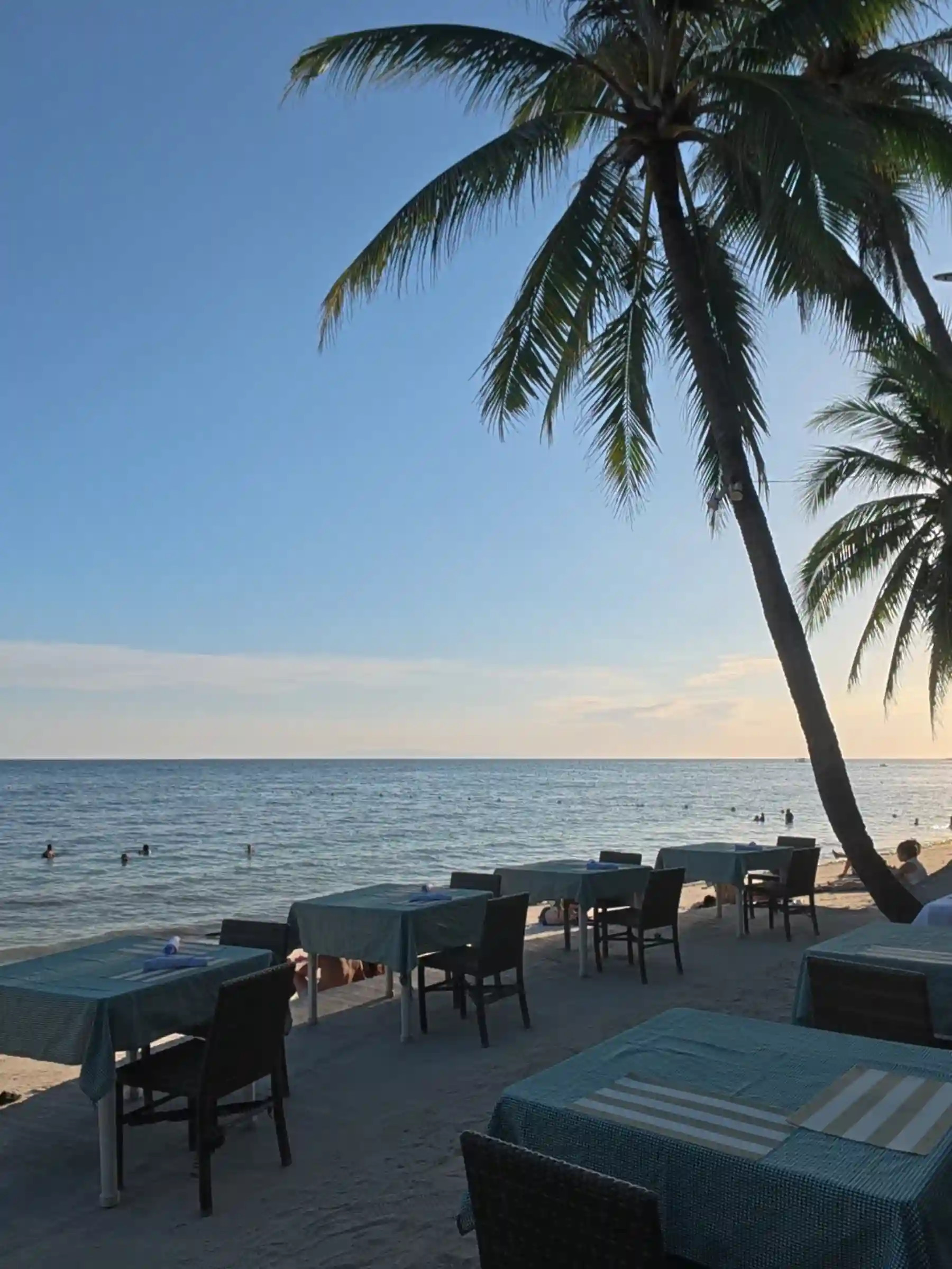 Teal clothed dining tables set on the sand beside a leaning coconut palm at a beachfront restaurant in Alona Beach Panglao Bohol at sunset