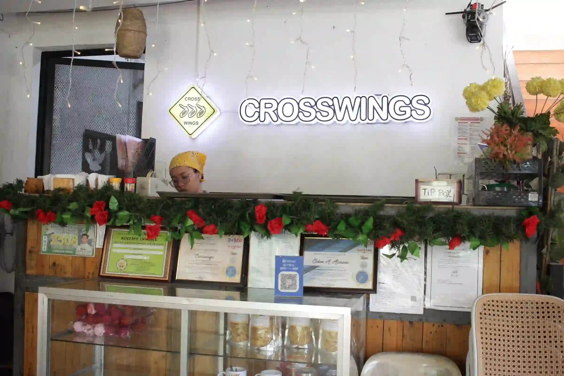 Crosswings illuminated neon sign above the service counter with a staff member and framed certificates in Alfonso Cavite