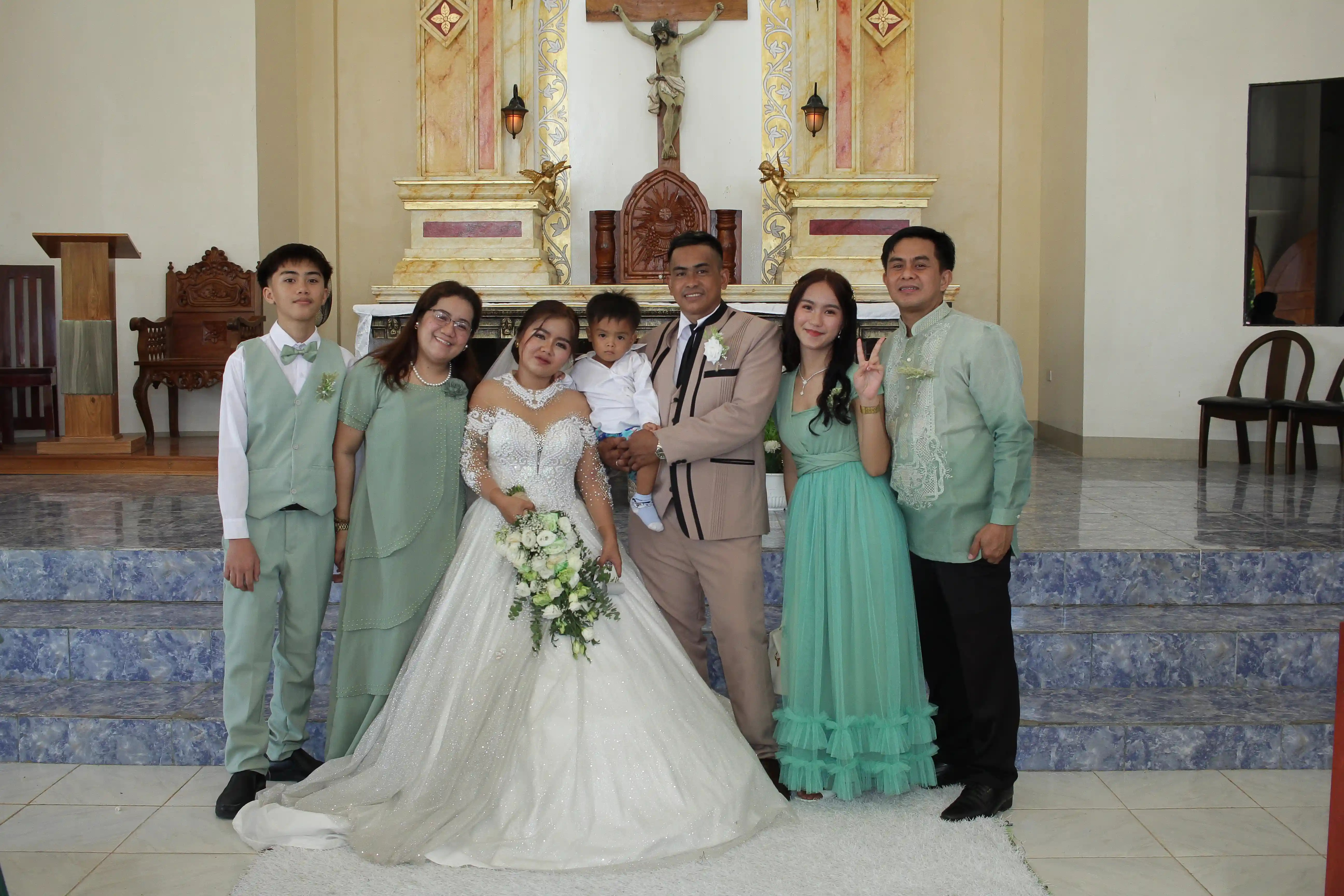 Ninong and Ninang Atanoza family posing with newlyweds John Aries Almendras and Lyka Isabel Bastida in front of the gilded altar of Our Lady of Fatima Mission Area in Socorro Oriental Mindoro