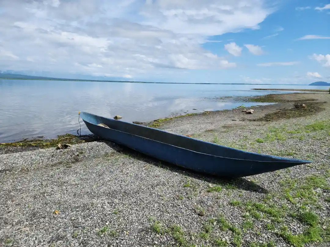 Blue canoe fishing boat resting on the gravel shore of Naujan Lake in Barangay Mabuhay II Socorro Oriental Mindoro with mountains in the background
