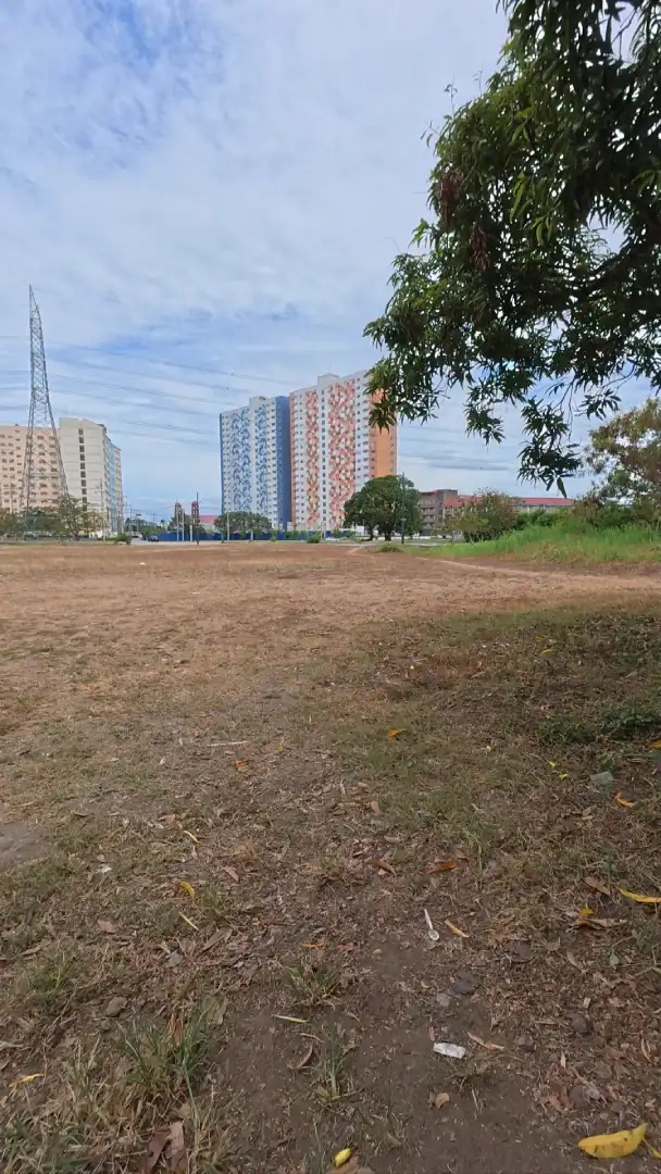 Open dry field with high rise condominium towers and a power line tower in the distance in Southwoods City