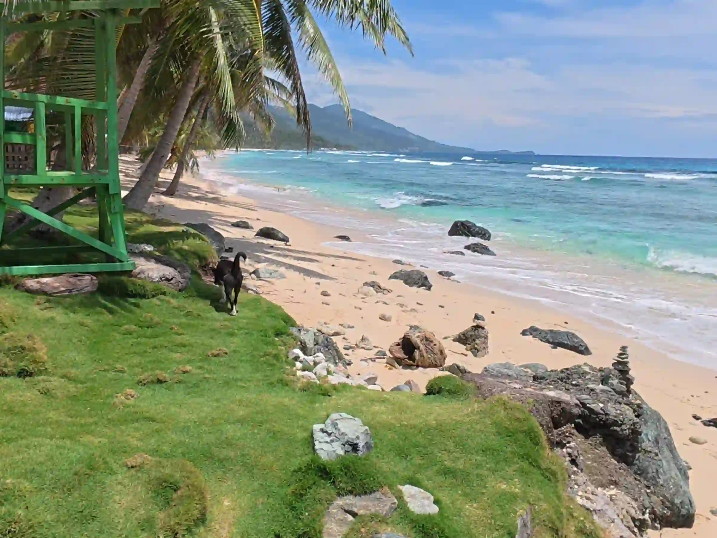 Wide view of turquoise ocean waves washing over creamy orange sand and black rock formations at Payag ni Jose beach in Lanca Mati Davao Oriental