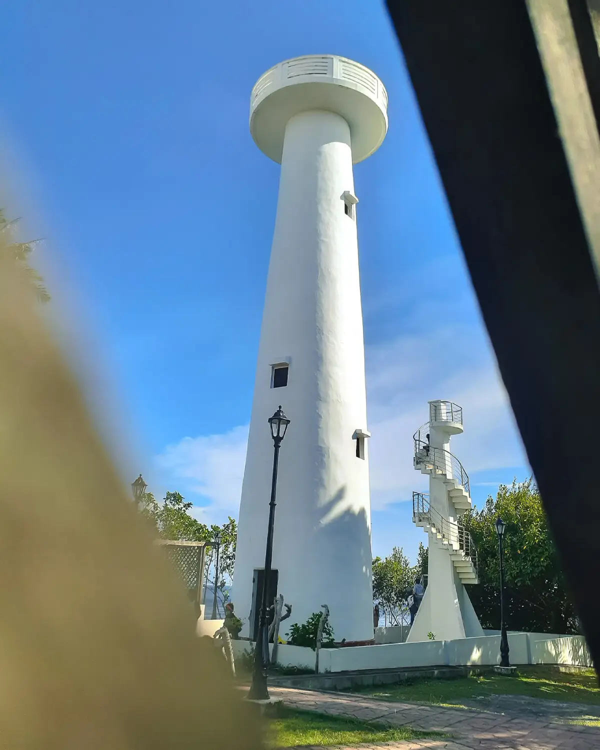 White cylindrical lighthouse tower at Cape San Agustin Parola in Governor Generoso Davao Oriental with an exterior spiral staircase brick pathways and maintained grounds photographed under a clear blue sky