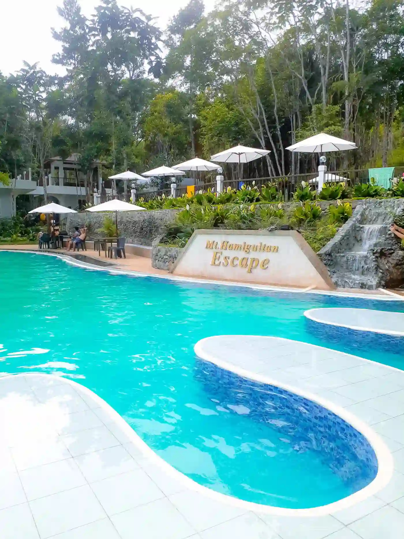 Wide view of the pool at Mt. Hamiguitan Escape Resort with the gold resort sign white market umbrellas and tables and chairs along the poolside in San Isidro Davao Oriental