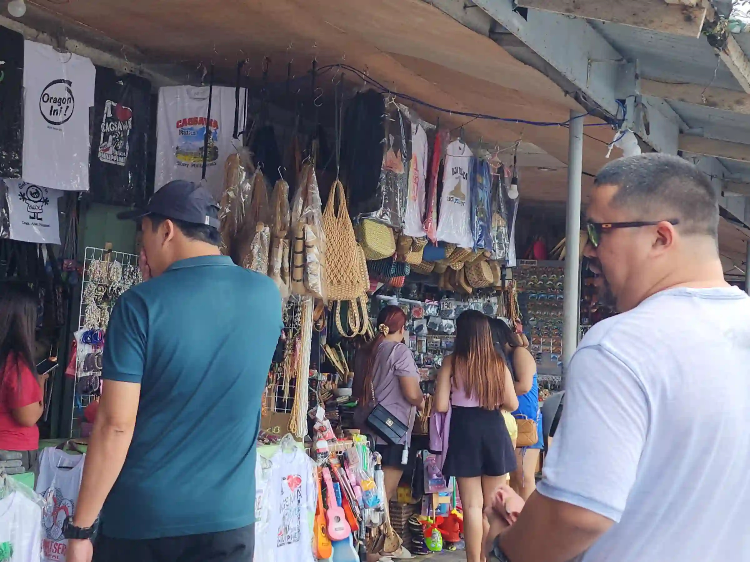 Jerwine Badiang and Alain Bibera browsing souvenir stalls selling shirts, woven bags and crafts under a corrugated roof near Cagsawa Ruins in Daraga Albay