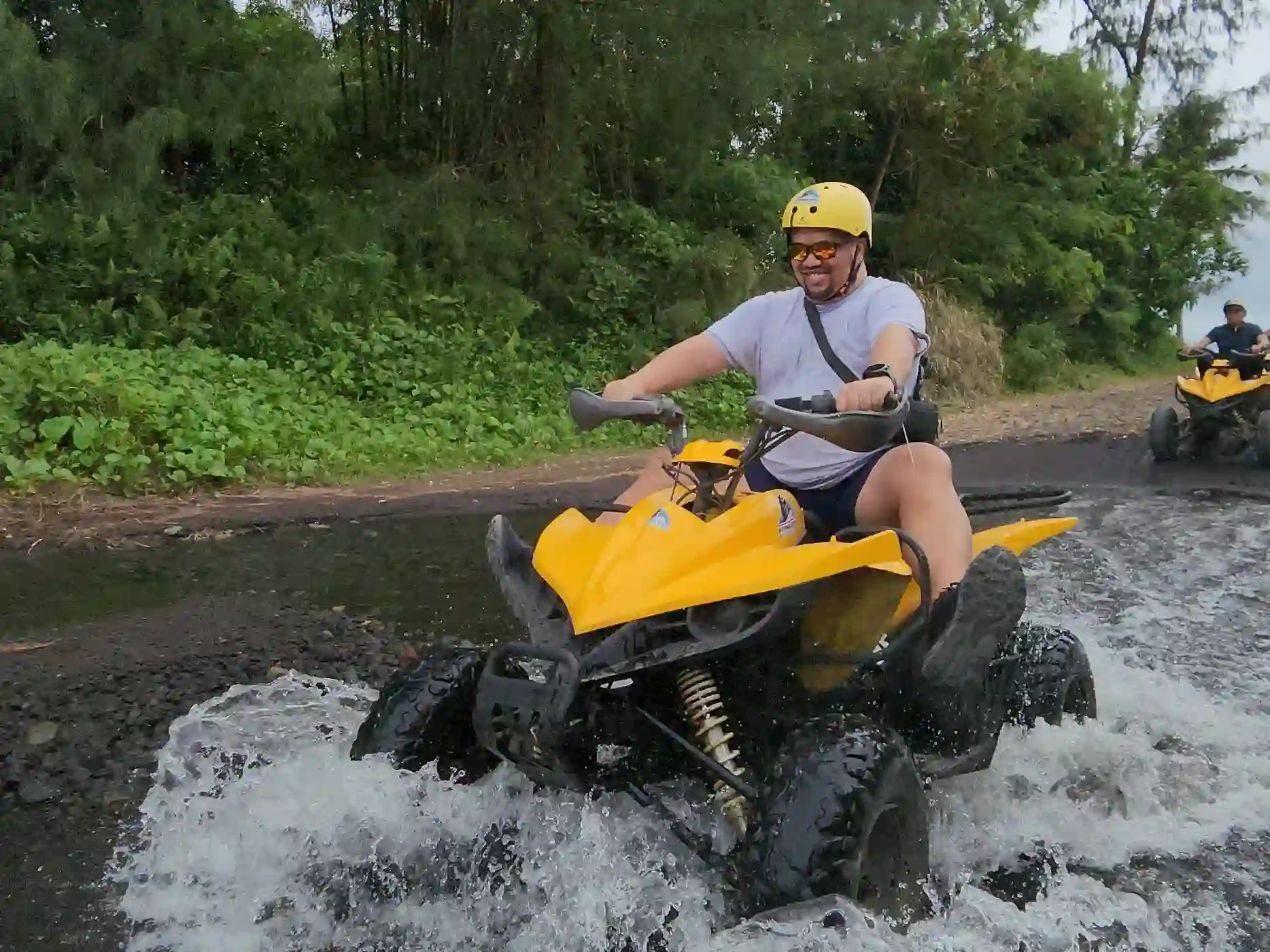 Alain Bibera in a yellow helmet on a yellow ATV sending up white water spray during a river crossing on the ATV trail to Green Lava in Daraga Albay