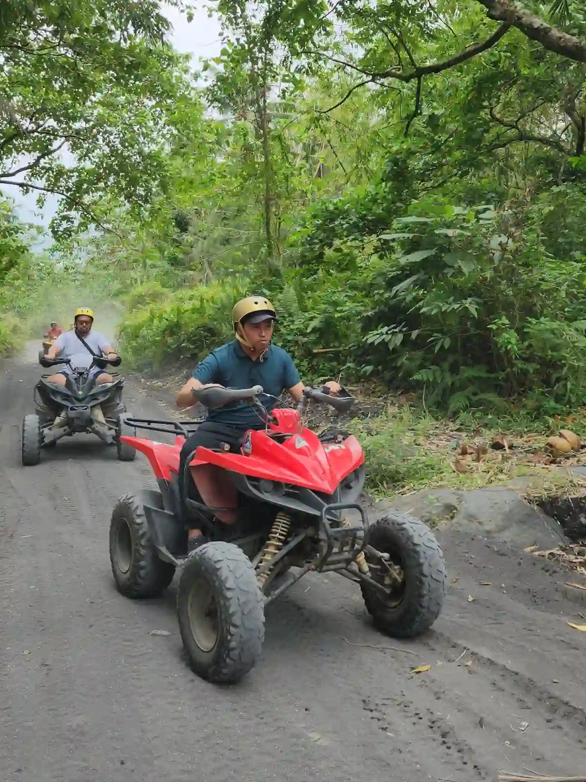 Two ATV riders navigating a narrow uphill trail through dense green forest on dark volcanic soil on the route to Green Lava near Mayon Volcano in Daraga Albay