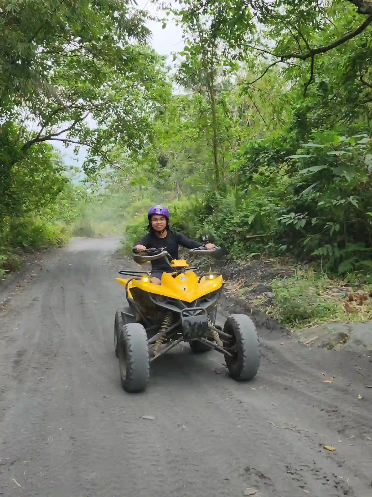 Nelmar Atanoza rider in a purple helmet on a yellow ATV on a dark volcanic soil trail through green forested terrain near Mayon Volcano in Daraga Albay
