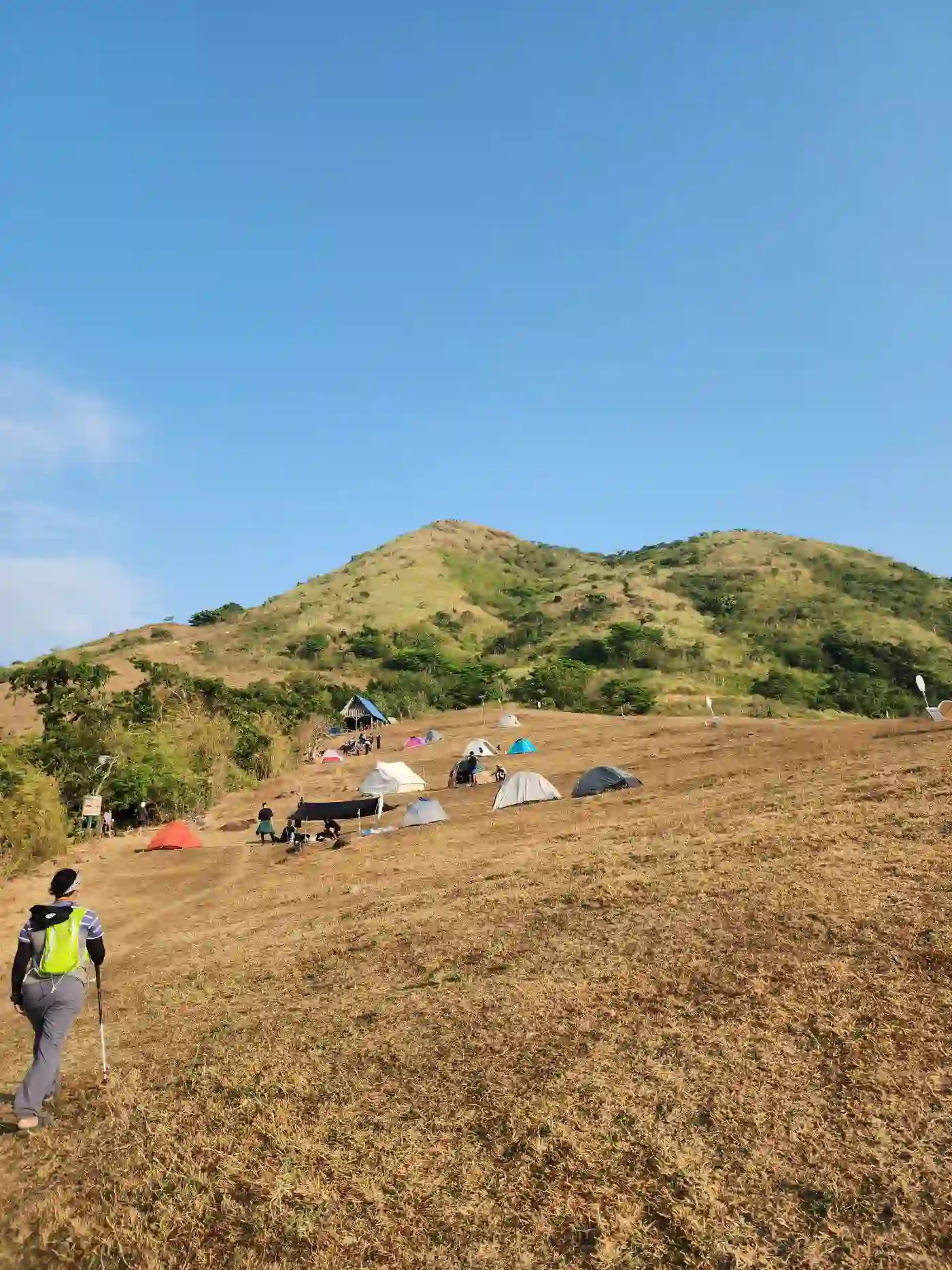 Scattered colorful camping tents on the lower slope of Mt. Talamitam with a bamboo rest hut visible and hikers moving around the camp in Nasugbo Batangas
