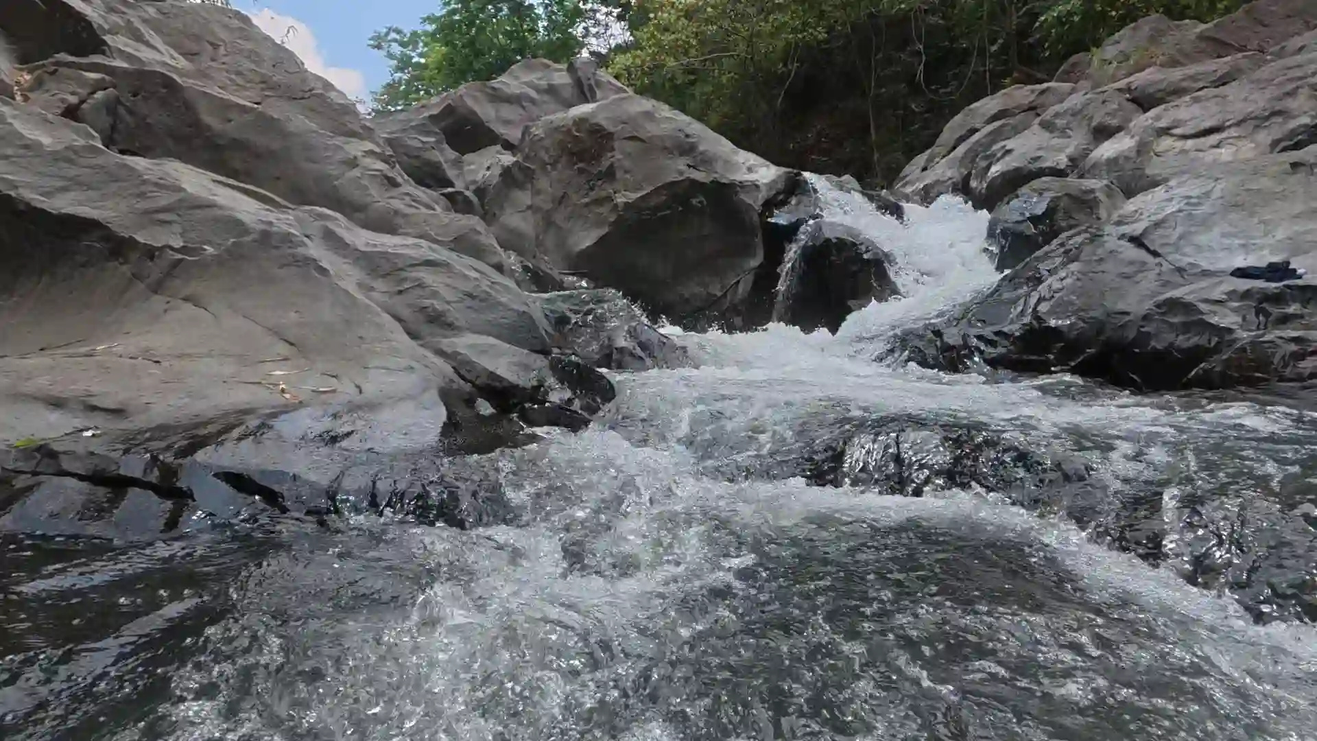 Fast moving river water rushing over large smooth dark boulders surrounded by dense green trees near the Mt. Talamitam jump-off area in Nasugbo Batangas