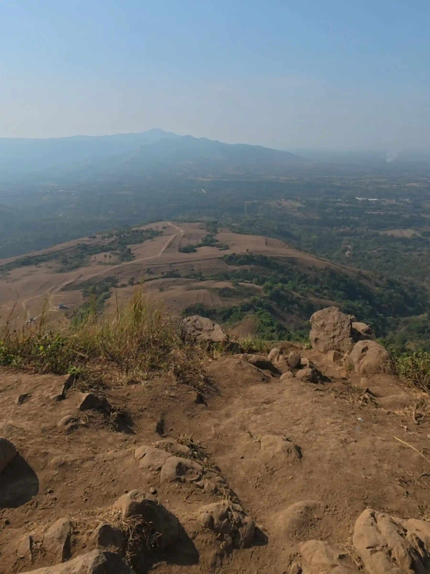 Wide aerial view from the summit of Mt. Talamitam showing the full rolling brown grassland descending into a wide hazy valley with layered mountain ranges in the background in Nasugbo Batangas