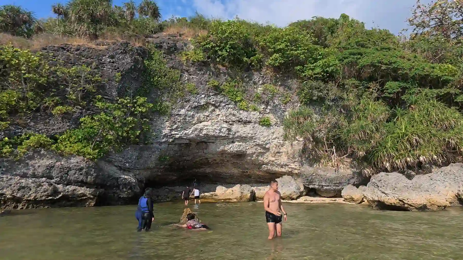 Limestone cliff face with a natural overhang and cave entrance at the waterline at Talim Beach in Matabungkay Lian Batangas with green vegetation growing through rock cracks