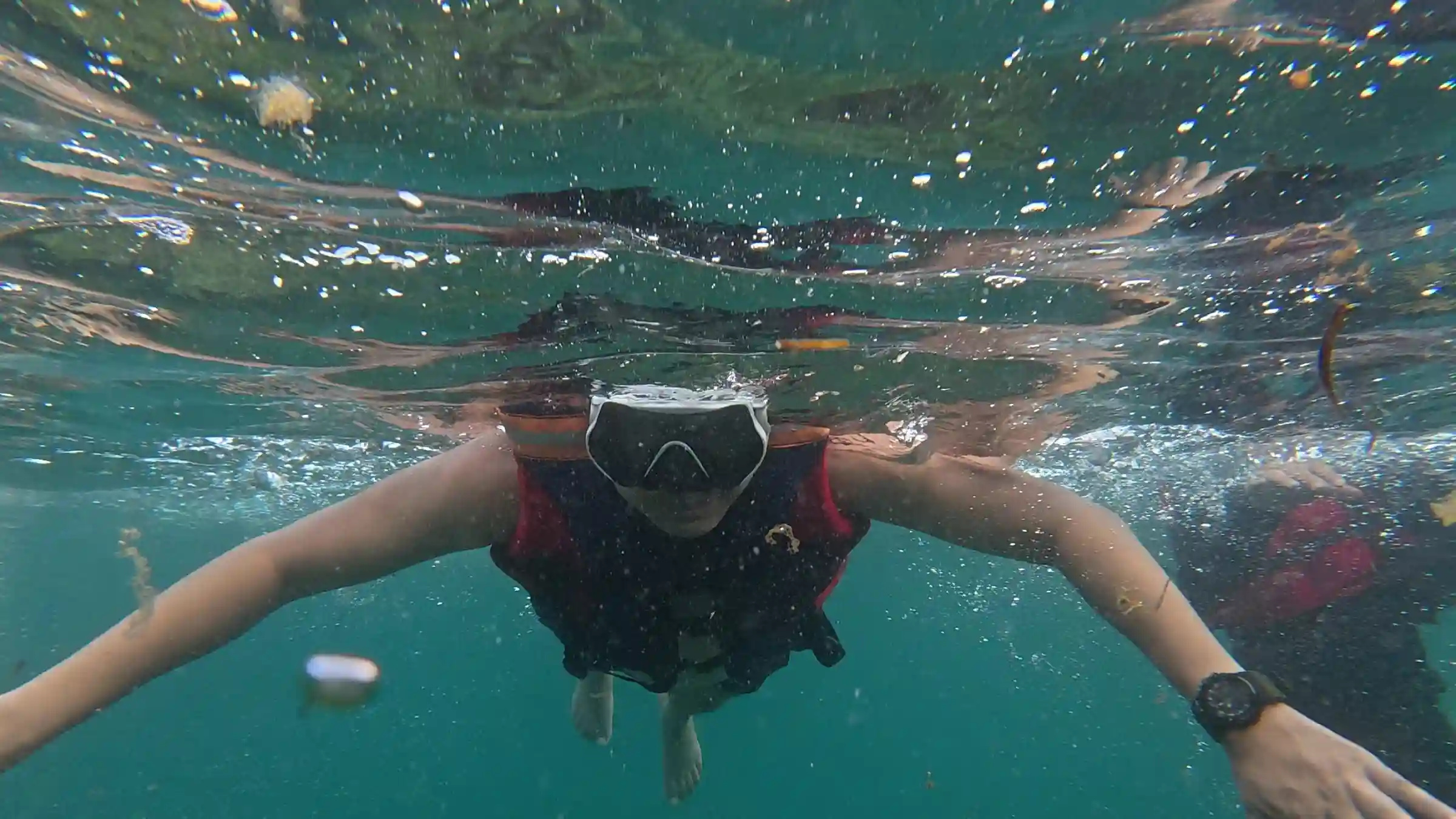Rencel Leyran a snorkeler wearing a dive mask and life jacket swimming underwater with arms spread at the reef near Matabungkay in Lian Batangas with turquoise water surrounding them