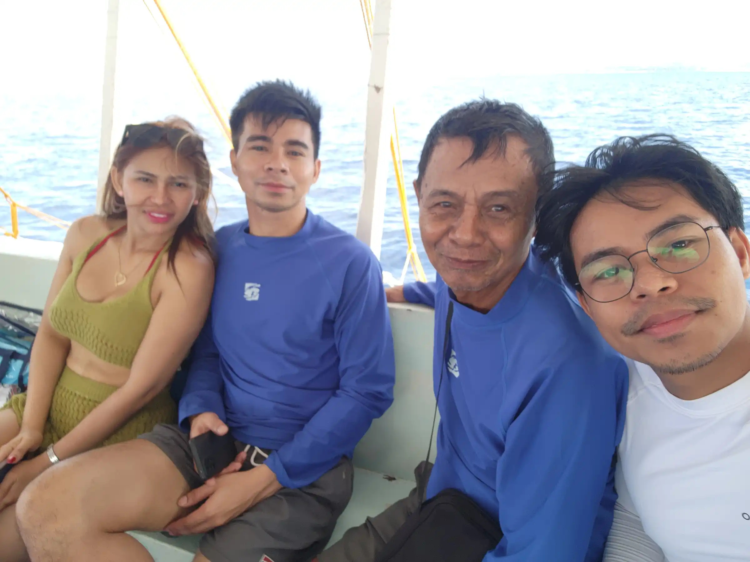 Group of four including two men in blue rashguards a woman and a younger man with glasses taking a selfie on a bangka at Balicasag Island Bohol
