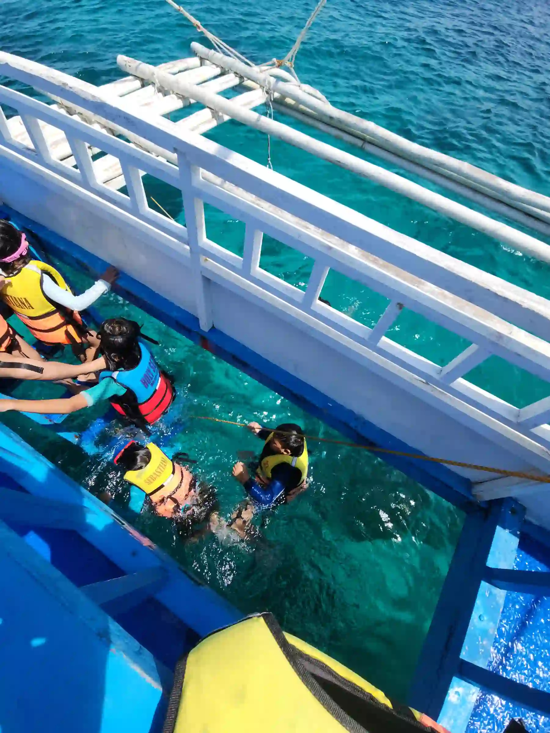Children in colorful life vests entering the water from the side of a bangka at Balicasag Island Bohol with turquoise water visible below