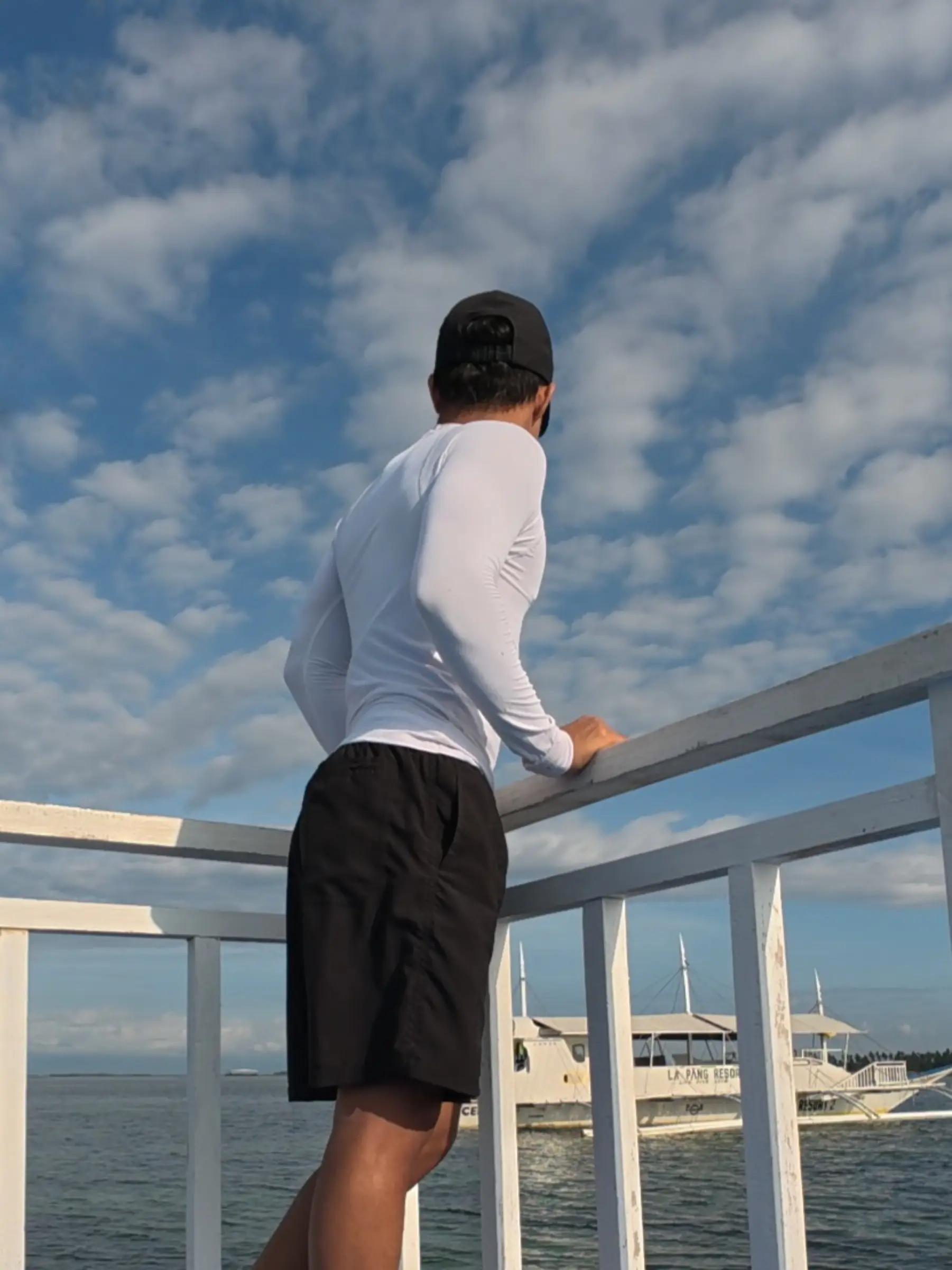 Traveler Nelmar Serondo Atanoza in white rashguard standing at the bow railing of a bangka with other boats and the ocean visible near Balicasag Island Bohol