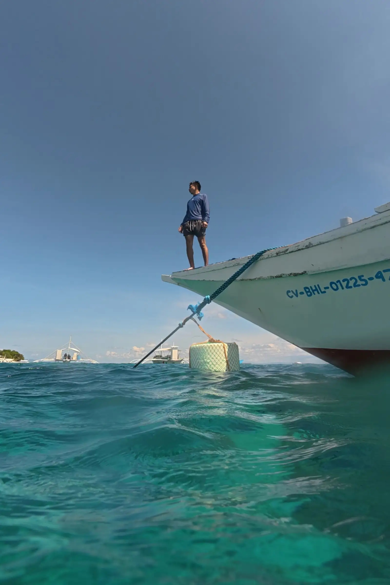 Traveler Marby Serondo Atanoza in blue rashguard standing at the prow of a moored bangka over clear green water at Balicasag Island Bohol