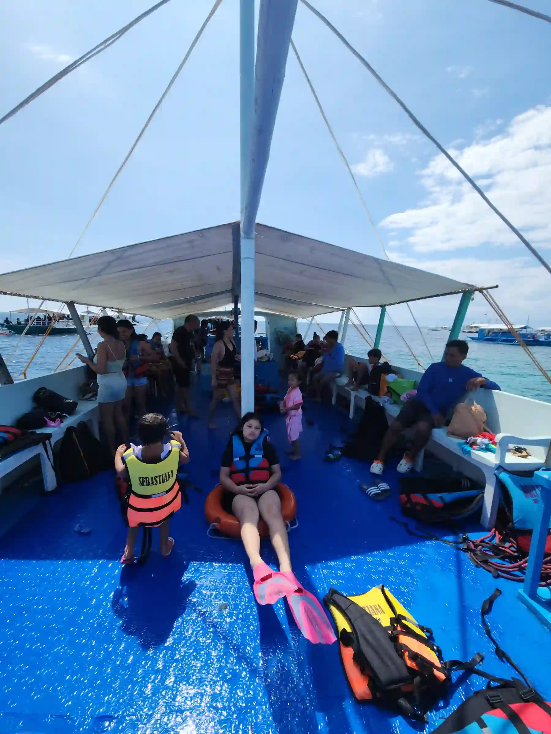 Crowded bangka deck with life vests fins and passengers resting at Balicasag Island Bohol with other boats visible on the water