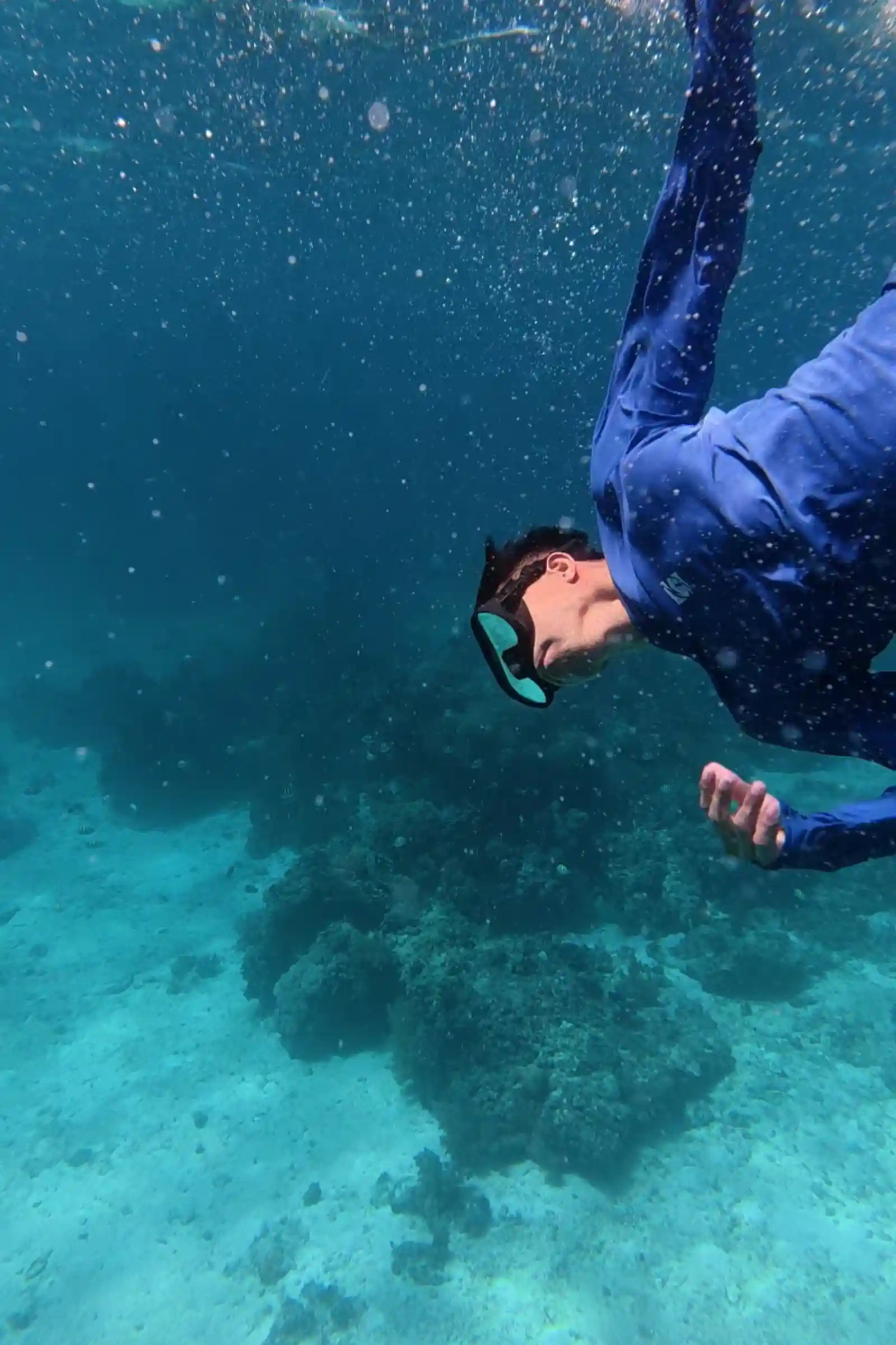Snorkeler Marby Serondo Atanoza in blue rashguard and mask descending head down toward coral reef formations in clear turquoise water at Balicasag Island Bohol