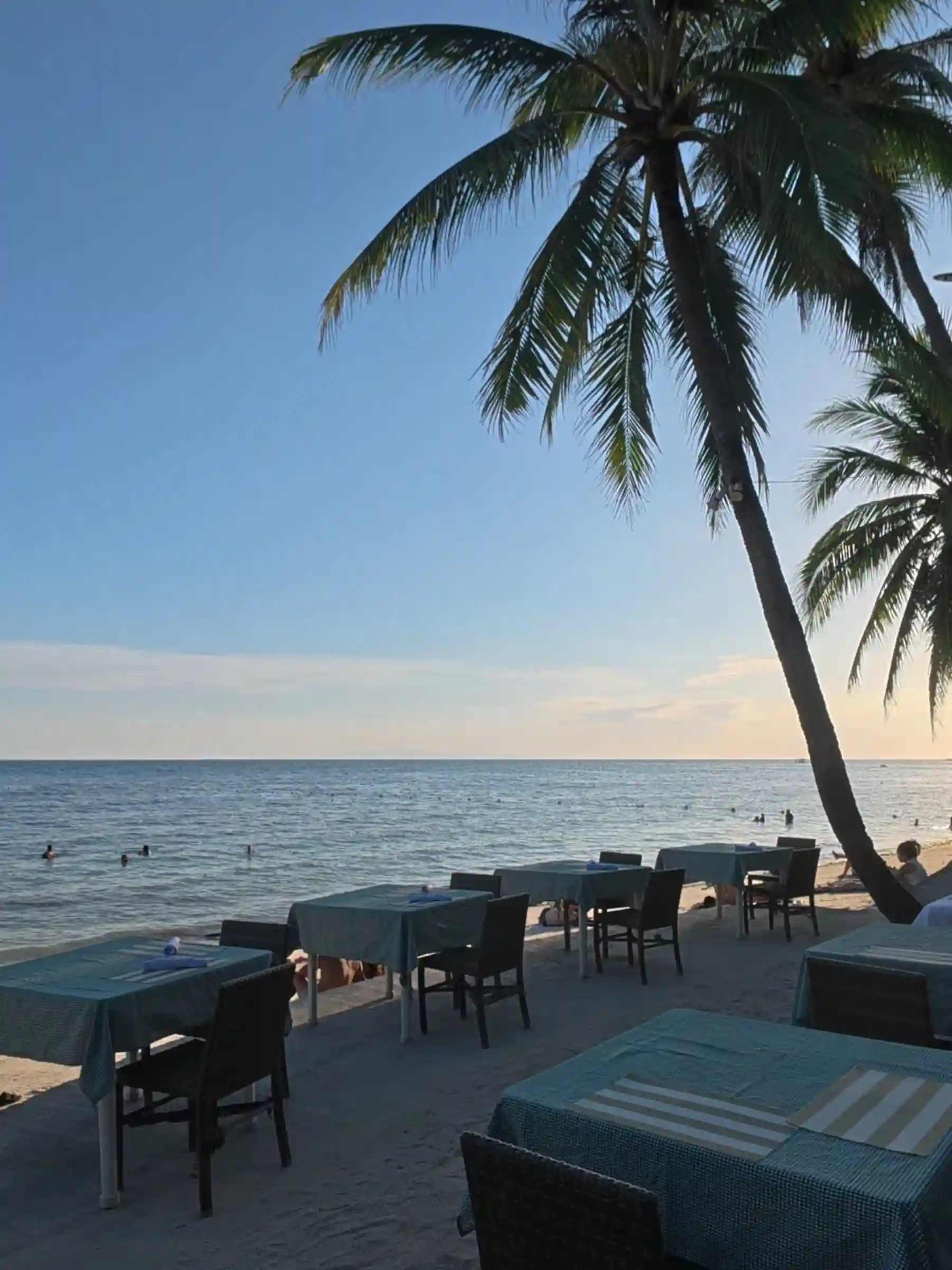 Teal clothed dining tables set on the sand beside a leaning coconut palm at a beachfront restaurant in Alona Beach Panglao Bohol at sunset