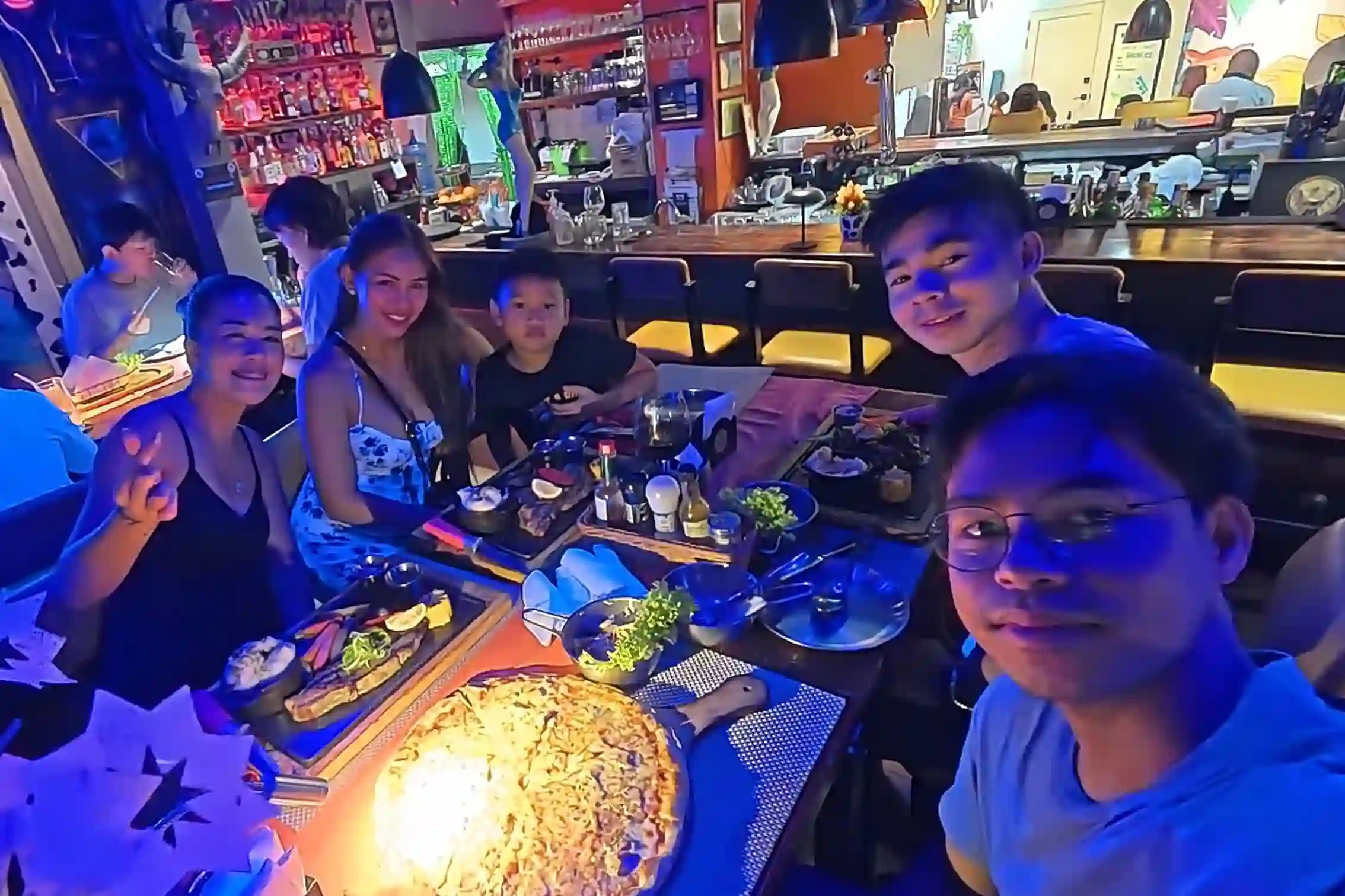Marby Atanoza and Angel Inangkilat with the group dining with steak and pizza on the table inside the blue lit interior of Max Cow restaurant in Alona Beach Panglao Bohol
