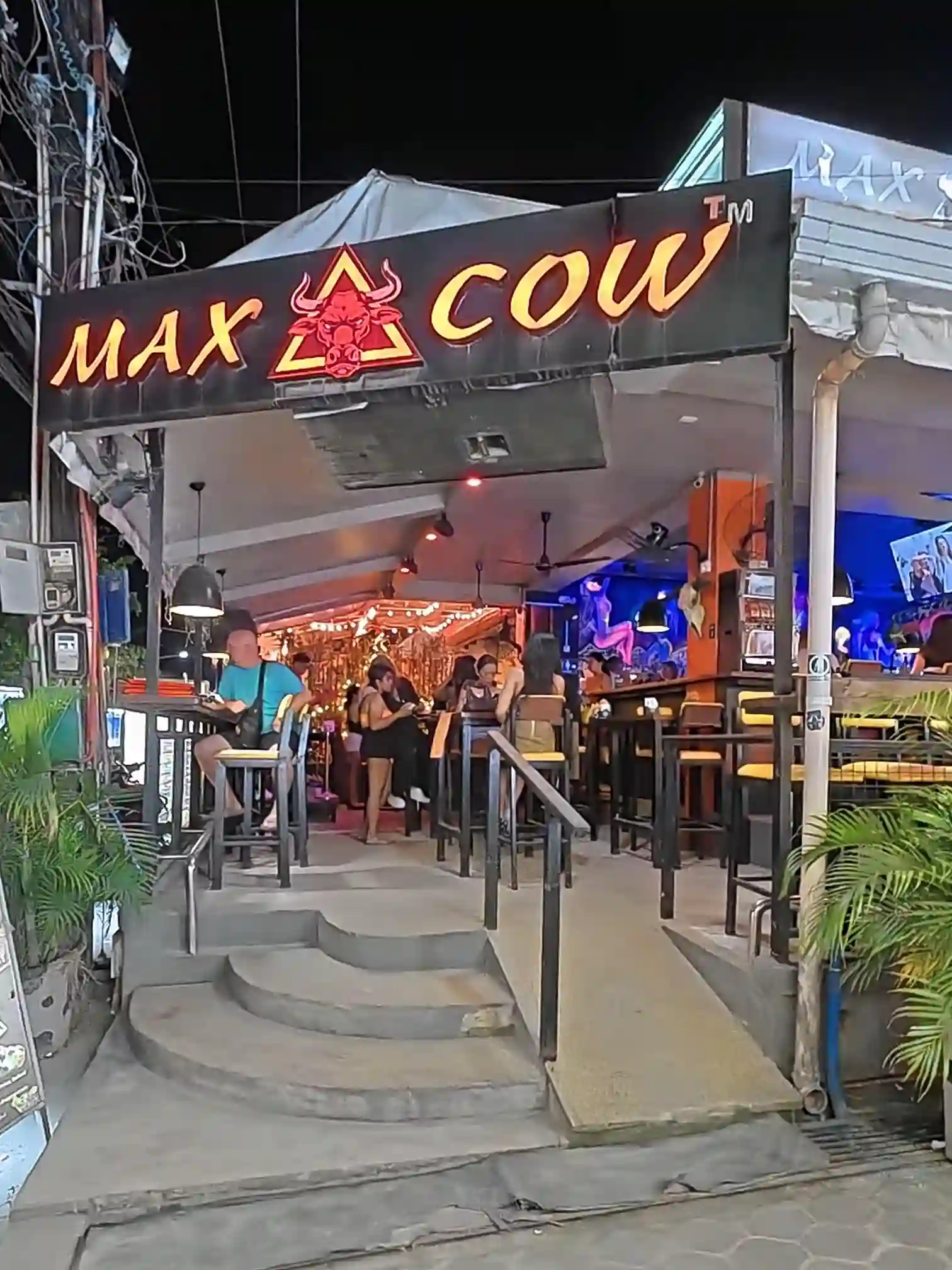 Illuminated Max Cow restaurant sign at night with diners seated at the entrance along the main street of Alona Beach Panglao Bohol
